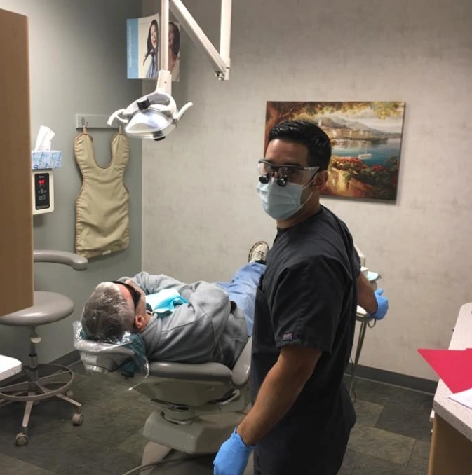 Dentist in protective gear examining patient in dental chair at Dr. Bob's Dental Care office.