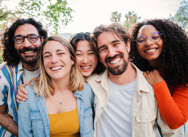 Five diverse smiling people posing together outdoors in casual clothing, appearing happy and friendly.