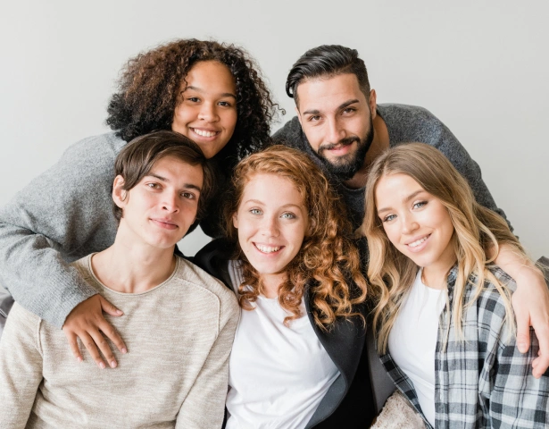 Five smiling people posing together for a portrait against a neutral gray background.