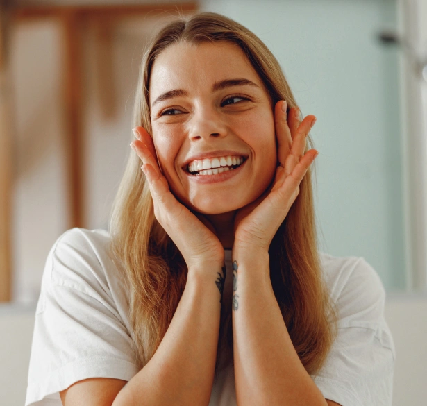 Happy woman smiling with hands to face in bright dental office setting.