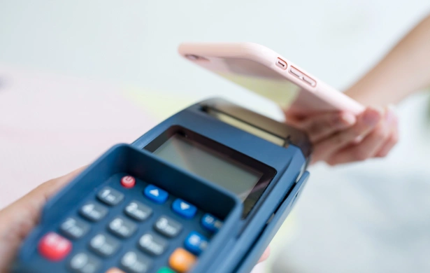 Person holding pink payment card over blue card reader machine for transaction processing.
