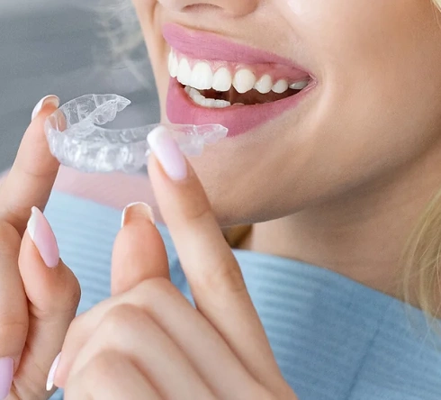 Woman smiling while holding clear aligner near her teeth for dental care treatment.