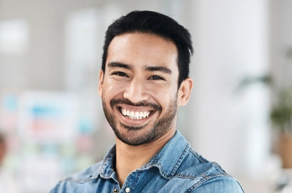 Smiling man in denim shirt at dental office with blurred background