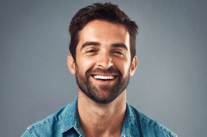 Smiling man in blue shirt against gray background, dental care professional portrait.