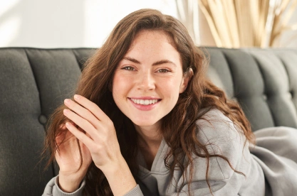 Smiling woman relaxing on gray couch in casual setting, promoting dental care wellness.