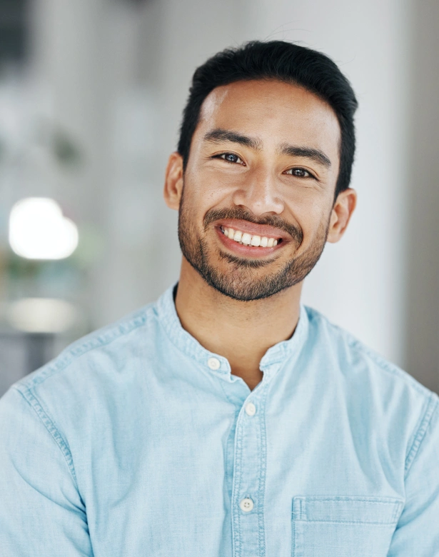 Smiling male dental professional in light blue shirt against blurred office background.