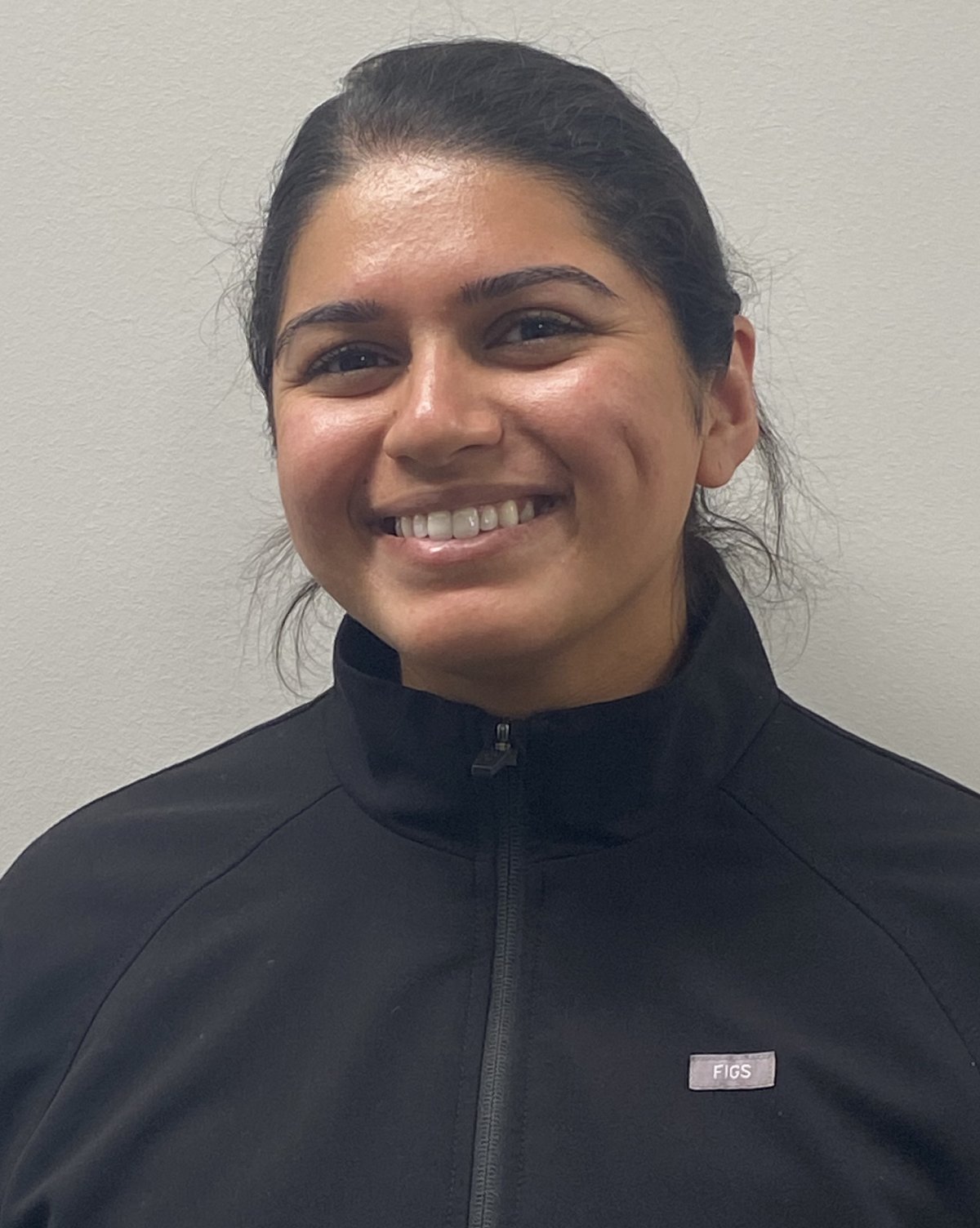 Smiling woman in black jacket against neutral background, professional headshot for dental care practice.