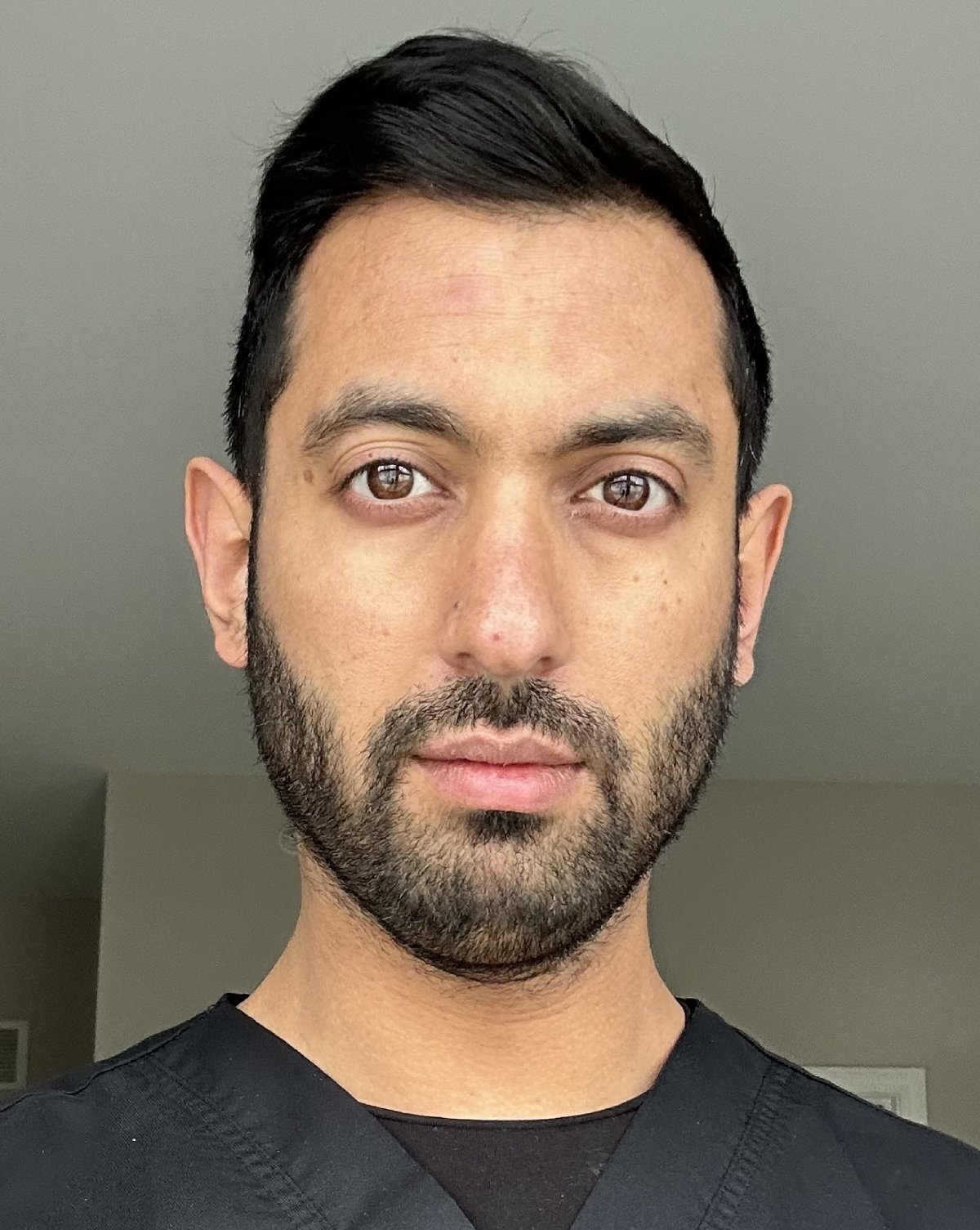 Professional headshot of male dental care professional against neutral gray background wearing dark shirt.