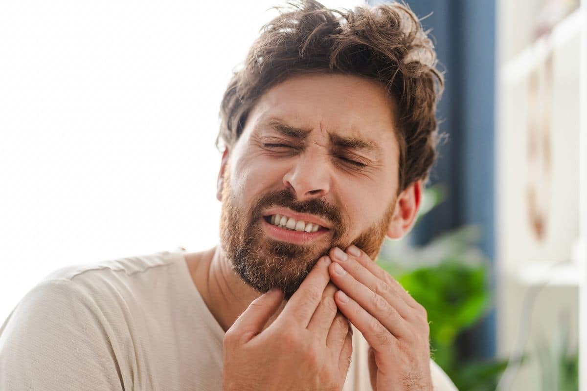 Man with beard experiencing tooth pain, holding his jaw in discomfort.