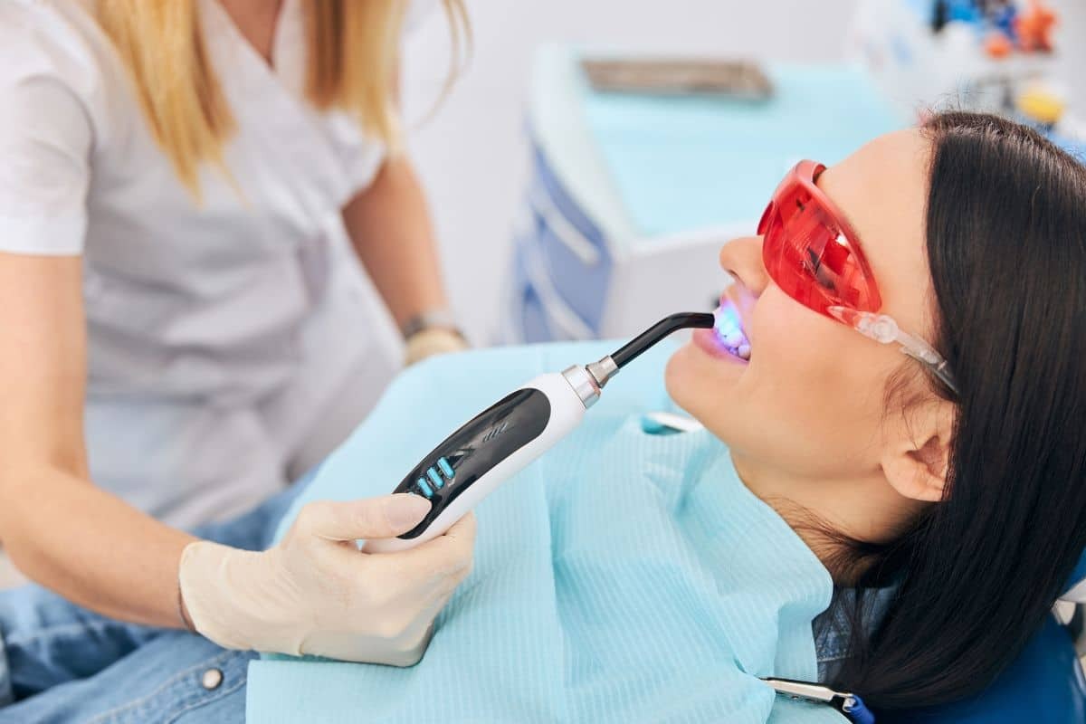 Dentist using UV whitening light on patient's teeth during professional whitening treatment.